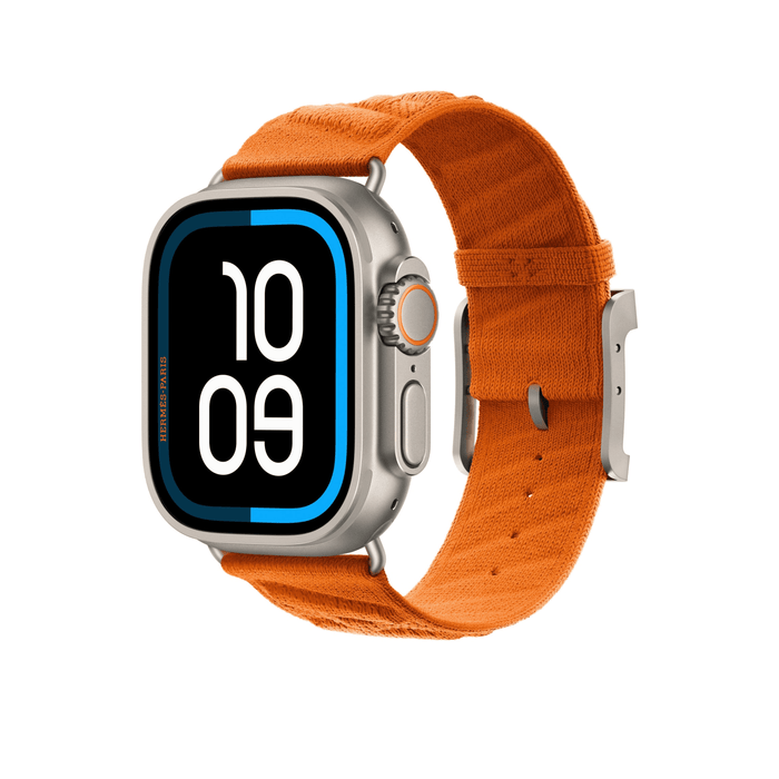 Orange Hermès En Mer band fitted to an Apple Watch Ultra, shown at an angle highlighting the textured fabric and titanium buckle.